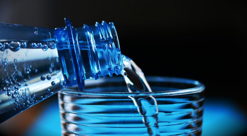 Acqua versata da una bottiglia in un bicchiere, simbolo delle analisi sull’acqua destinata al consumo umano